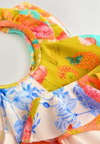 Haut de maillot de bain floral multicolore avec un tissu texturé, des bords à volants et un mélange vibrant de motifs roses, bleus, oranges et verts.