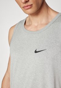 Camiseta atlética sin mangas en gris, hecha de una tela suave, con el logo de Nike en negro en el pecho; escote redondo y un ajuste sin estructura.