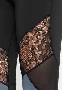 Leggings neri con dettagli in pizzo e pannelli in rete, caratterizzati da un design geometrico in tonalità contrastanti di nero e blu.