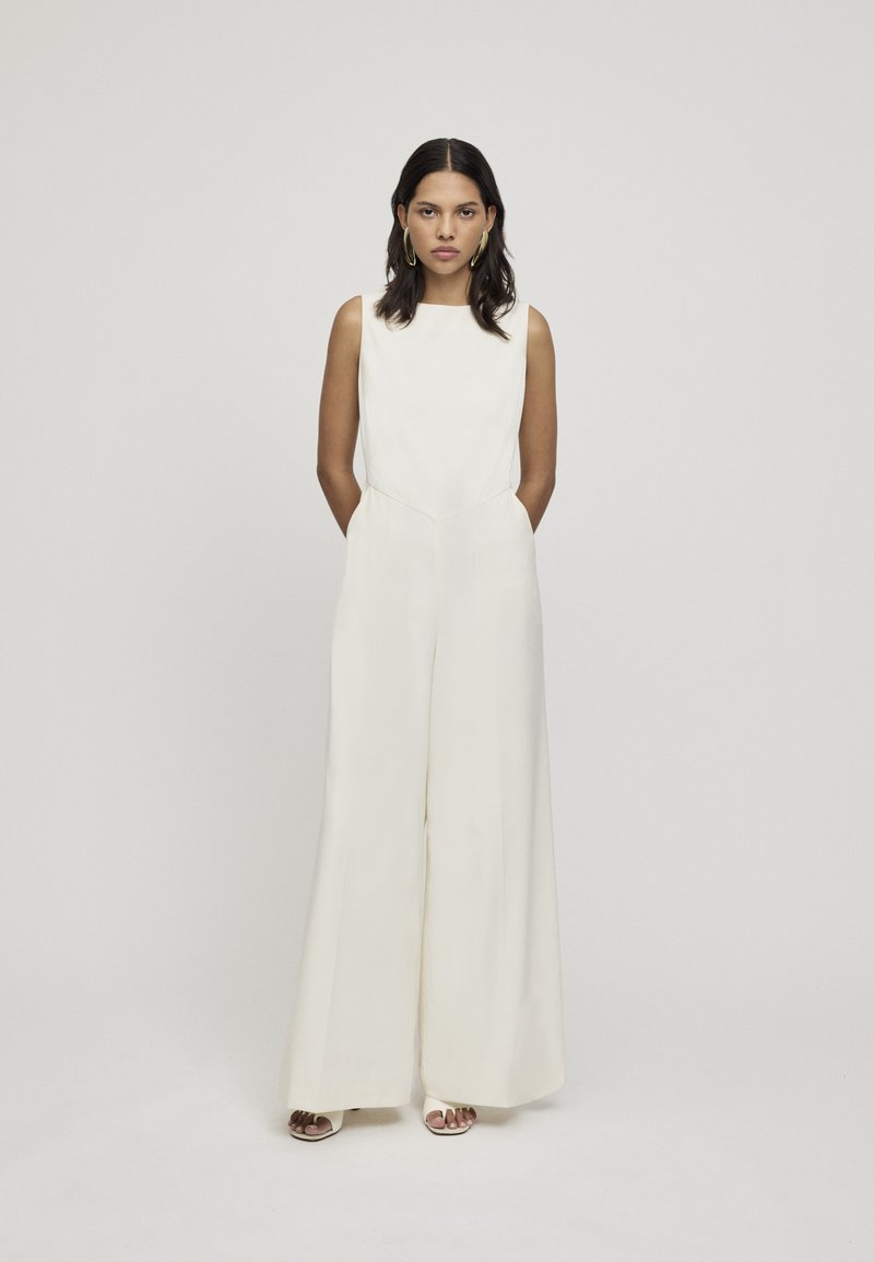 Crème-kleurige jumpsuit met een nauwsluitend lijfje en een ontwerp met wijde benen. Gemaakt van zachte stof, met een vierkante halslijn en subtiele stikdetails.