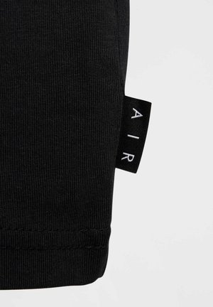 Tejido de algodón negro con una textura acanalada, que presenta una etiqueta con la inscripción "AIR" en blanco sobre un fondo negro, mostrando detalles de diseño minimalistas.