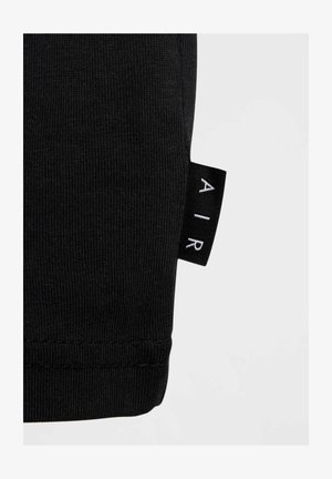 Tejido de algodón negro con una textura acanalada, que presenta una etiqueta con la inscripción "AIR" en blanco sobre un fondo negro, mostrando detalles de diseño minimalistas.