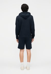 Marinblå hoodie med känguruficka och matchande shorts. Bomullstyg, normal passform, ribbade muddar och fåll, tillsammans med vita detaljerade strumpor och sneakers.
