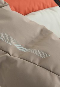 Tissu de doudoune beige avec une texture lisse ; présente un motif géométrique subtil et un graphique gris clair le long de la couture.