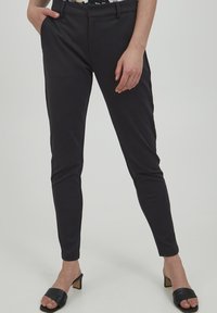 Mustad kootud püksid sujuva tekstuuri, kitsaste lõigetega ja elastse vöökohaga. Kanda mustade kontsadega sandaalidega.