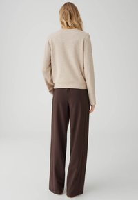 Beige sweatshirt met lange mouwen en ronde hals, gecombineerd met brede bruine broekspijpen, met een zachte textuur en een losse pasvorm.