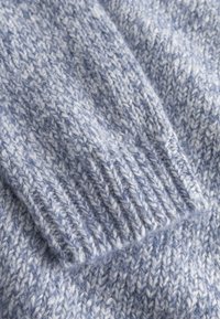 Gestrickter Pullover aus hellblauem und weißem Garn, der ein strukturiertes Muster mit gerippten Ärmeln und einer weichen, flauschigen Oberfläche zeigt.