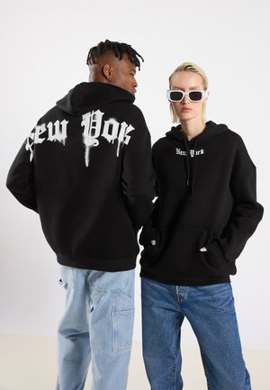 Black hoodies featuring "New York" in white, with dripped font design. Pairing light blue and dark blue jeans, showcasing relaxed fits.