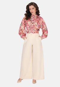 Bluză cu model floral în nuanțe de roz, cu detalii cu nasturi și mâneci bufante, asociată cu pantaloni evazați crem cu talie înaltă.