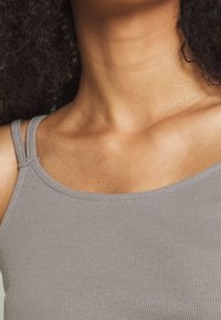 Top in maglia grigia a costine con spalline sottili, caratterizzato da un collo a barchetta e una superficie liscia, parte del tessuto si adagia delicatamente attorno alla clavicola.