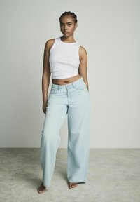 Jean large bleu clair à taille haute, associé à un débardeur blanc à côtes. Texture de tissu lisse et coupe décontractée.