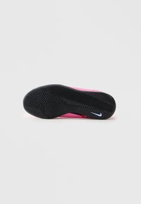 Fekete textúrájú talpú rózsaszín Nike cipő, fehér Nike swoosh logóval, sima világos háttérrel.