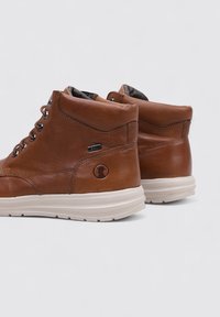 Bottines en cuir marron avec bout rond, semelle en caoutchouc crème contrastante, œillets en métal et logo embossé à l'arrière.