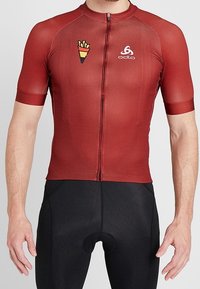 Rød kortærmet cykeltrøje med tekstureret stof, lynlås foran og logo. Tætsiddende design kombineret med sorte cykelshorts.