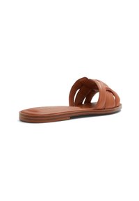 Sandale en cuir marron, à semelle plate et avec des brides entrecroisées, au design minimaliste. Texture lisse avec un subtil éclat.