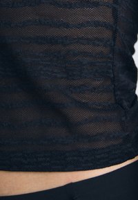 Black mesh top featuring a textured pattern with wavy lines, highlighting a sheer design and a fitted silhouette.
