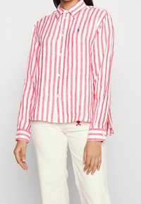 Camisa de manga larga a rayas rojas y blancas con cuello, que presenta un pequeño logo, fabricada en tejido liviano.