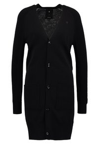 Long cardigan noir avec col en V, manches côtelées et poches, fermeture boutonnée à l'avant et longueur mi-cuisse.