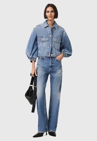 Giacca in denim di colore azzurro chiaro, corta, con maniche a sbuffo e chiusura frontale con bottoni, abbinata a jeans blu chiaro larghi e accessori neri.