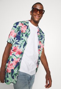Kurzärmliges, knöpfbares Hemd mit navy Hintergrund und großen rosa Blumenmustern sowie grünen Blättern, aus leichtem Stoff gefertigt.