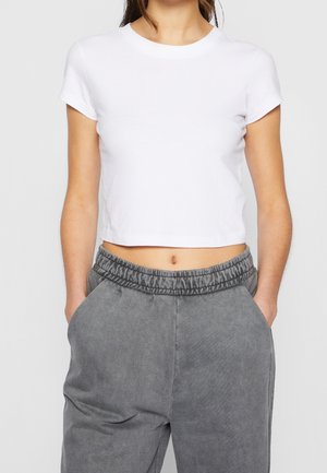 Camiseta corta blanca de algodón con mangas cortas y cuello redondo, combinada con pantalones grises con cordón y bolsillos laterales.