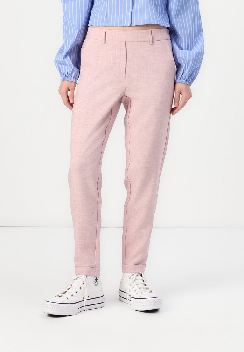 Personne portant un pantalon sur mesure rose pâle, des baskets montantes blanches et une chemise à manches longues rayée bleue avec des poignets élastiques.