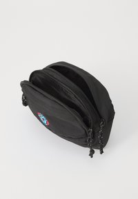Saco de nylon preto com dois compartimentos com fecho éclair, de forma arredondada, e um patch bordado colorido na frente. Exterior texturizado, fechos robustos.