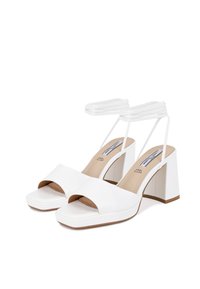 Sandali bianchi con tacco alto a blocco, design con punta aperta e cinturini incrociati alla caviglia. Superficie liscia, stile minimalista.
