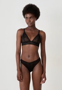 Soutien-gorge en dentelle noire et string assorti avec un design triangulaire, des bords festonnés et des motifs géométriques complexes tout au long.