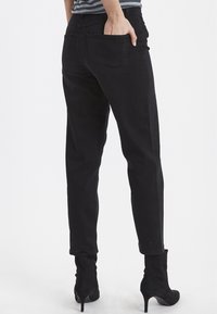 Vaqueros de mezclilla negra de corte holgado, con bolsillos traseros y puños enrollados, combinados con botas negras de tacón alto.