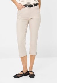 Beige cropped broeken van gladde stof, met een middelhoge taille en zijsplitten aan de zoom, gecombineerd met zwarte mesh platte schoenen.