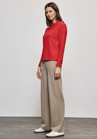 Rotes Langarmoberteil mit strukturiertem Finish, kombiniert mit hellbeigen weiten Hosen und weißen Turnschuhen, die ein einfaches Design aufweisen.