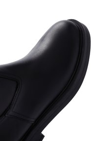 Stivale alla caviglia in pelle nera con punta arrotondata, texture liscia, dettagli di cucitura sottili e suola piatta in gomma. Nessun hardware o accentuazione visibile.