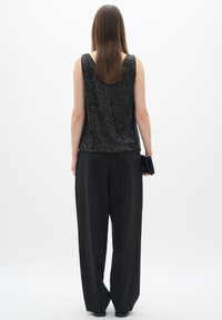 Top senza maniche nero con paillettes, pantaloni neri larghi, design minimalista, texture liscia, lucentezza sottile, abbinato a una piccola clutch nera.