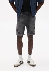 Șorturi din denim gri cu accente distruse, manșete răsucite și un design cu cinci buzunare. Poartă încălțăminte albă sport și șosete albe până la gleznă.