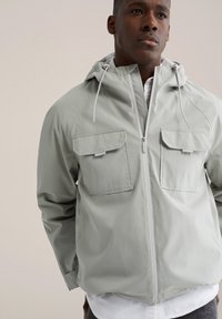 Lichtgrijs gewatteerd jack met capuchon, twee borstzakken, een ritssluiting aan de voorkant en verstelbare trekkoorden. Gladde, waterbestendige stof met een ontspannen pasvorm.