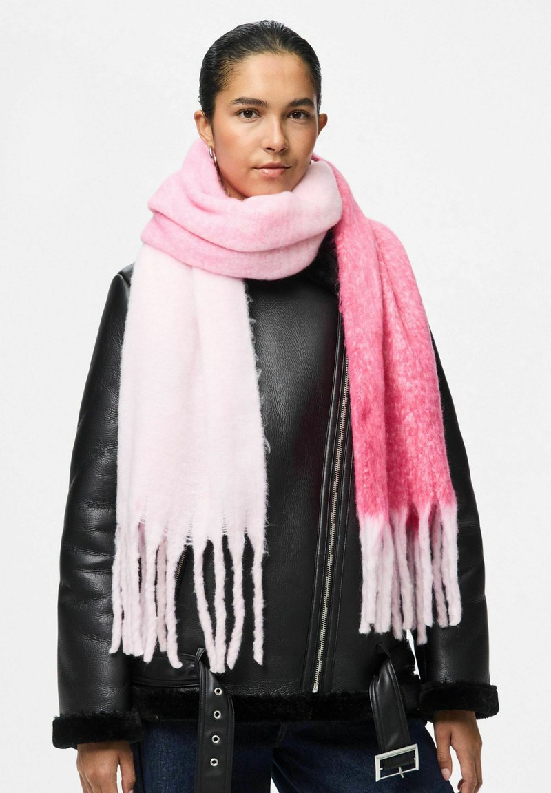 Rosa ombré tørklæde lavet af blødt stof, med frynsede kanter. Båret over en sort læderjakke, med en skinnende tekstur og afslappet fald.
