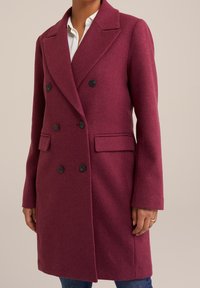 Cappotto doppiopetto in lana color bordeaux con rever a incavo, quattro bottoni neri, due tasche frontali e maniche lunghe.