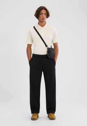 Polo crema a maniche corte, pantaloni neri larghi, stivali gialli in pelle e una borsa a tracolla nera con superficie texturizzata.