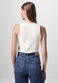 Witte mouwloze top met een zachte textuur, gecombineerd met high-waisted donkerblauwe spijkerbroek met een leren label en twee achterzakken.