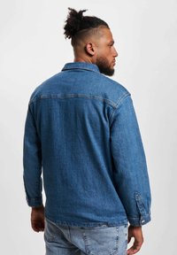 Denimjakke i mellomblått, med krage, lange ermer og knappede mansjetter. Strukturert stoff med et lett slitt utseende.