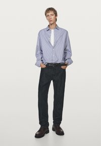 Striped, long-sleeve shirt in light blue and white, paired with dark denim jeans. Brown leather shoes complete the outfit.