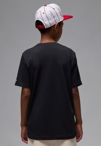 T-shirt en coton noir à manches courtes, vu de dos. Couleur unie sans motifs ni designs visibles, porté par une personne.