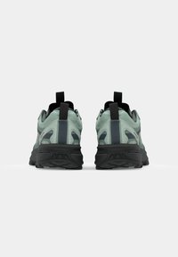 Zielono-czarne sneakersy z teksturowaną siateczkową cholewką, pętlami na pięcie i masywną czarną podeszwą. Charakteryzują się nowoczesnym stylem.