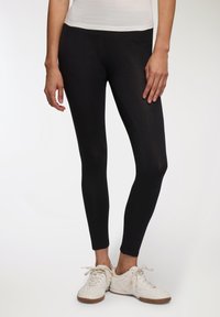 Czarne legginsy z elastycznego materiału, o gładkiej fakturze, dopasowanym kroju i prostym designie. Połączone z białymi butami sportowymi.