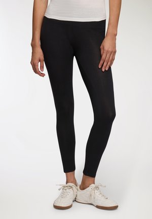 Leggings neri realizzati in tessuto elasticizzato, con una texture liscia, una forma aderente e un design semplice. Abbinati a scarpe da ginnastica bianche.