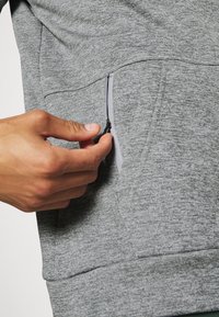 Harmaa huppari, jossa on tekstuuri, sivussa vetoketjullinen tasku, jota korostaa kontrastivärinen vetoketjureunus.