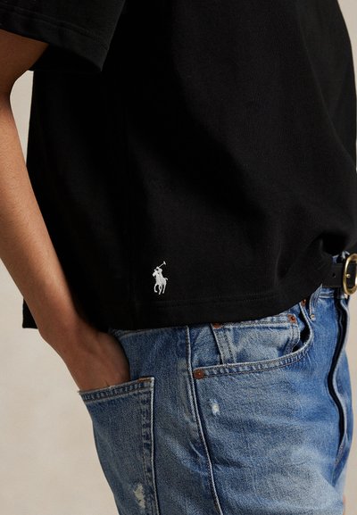 Inimene kannab musta lühikeste varrukatega särki, millel on väike valge hobuselogo ääre lähedal, särk on sisse toppitud sinistesse teksadesse musta vööga.