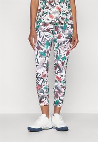 Capri-Leggings mit einem abstrakten, bunten Muster aus Rot, Grün und Schwarz auf weißem Hintergrund, kombiniert mit weißen Sportschuhen.