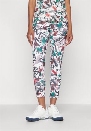 Capri-Leggings mit einem abstrakten, bunten Muster aus Rot, Grün und Schwarz auf weißem Hintergrund, kombiniert mit weißen Sportschuhen.